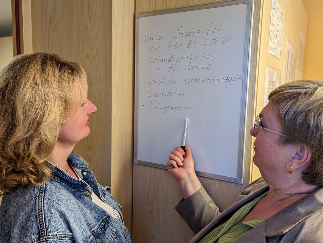 Zwei Frauen stehen vor einem Whiteboard, eine zeigt mit einem Stift auf handschriftlichen Text zu einem Auslandspraktikum in der Schweiz.