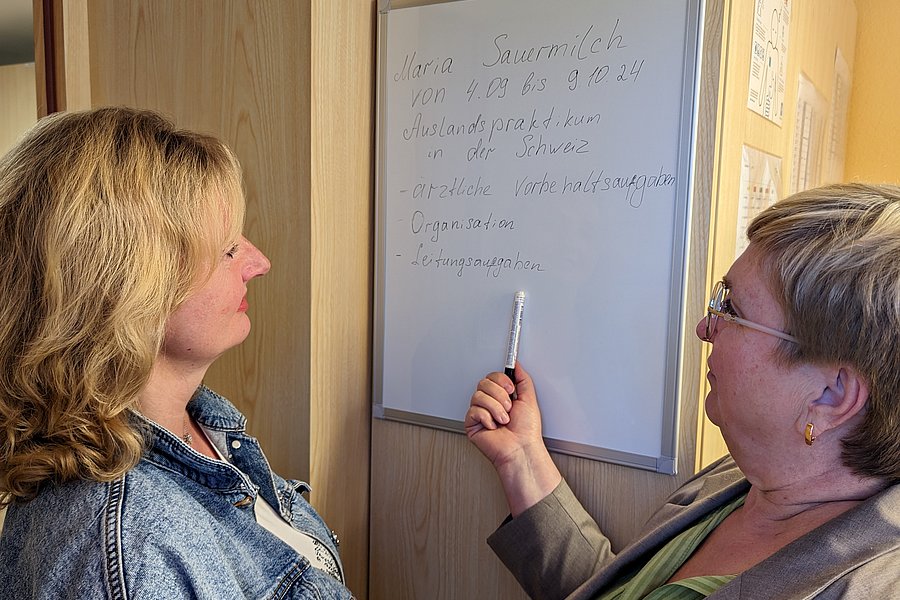Zwei Frauen stehen vor einem Whiteboard, eine zeigt mit einem Stift auf handschriftlichen Text zu einem Auslandspraktikum in der Schweiz.